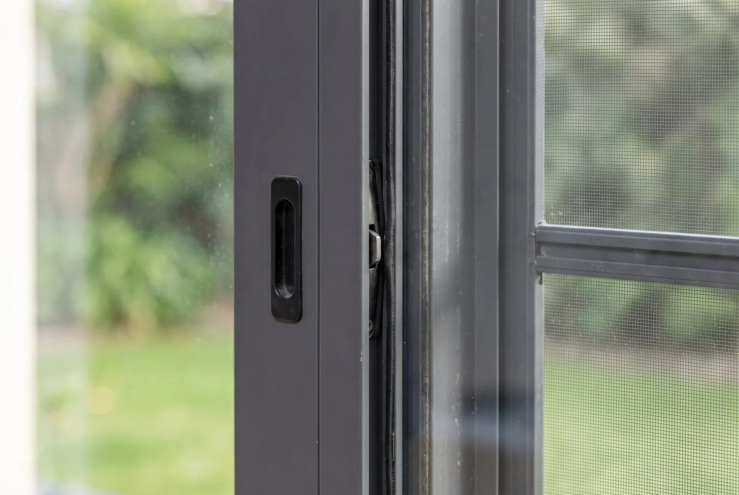 Close-up of an aluminium sliding window meeting rail, mosquito-mesh track and handle
